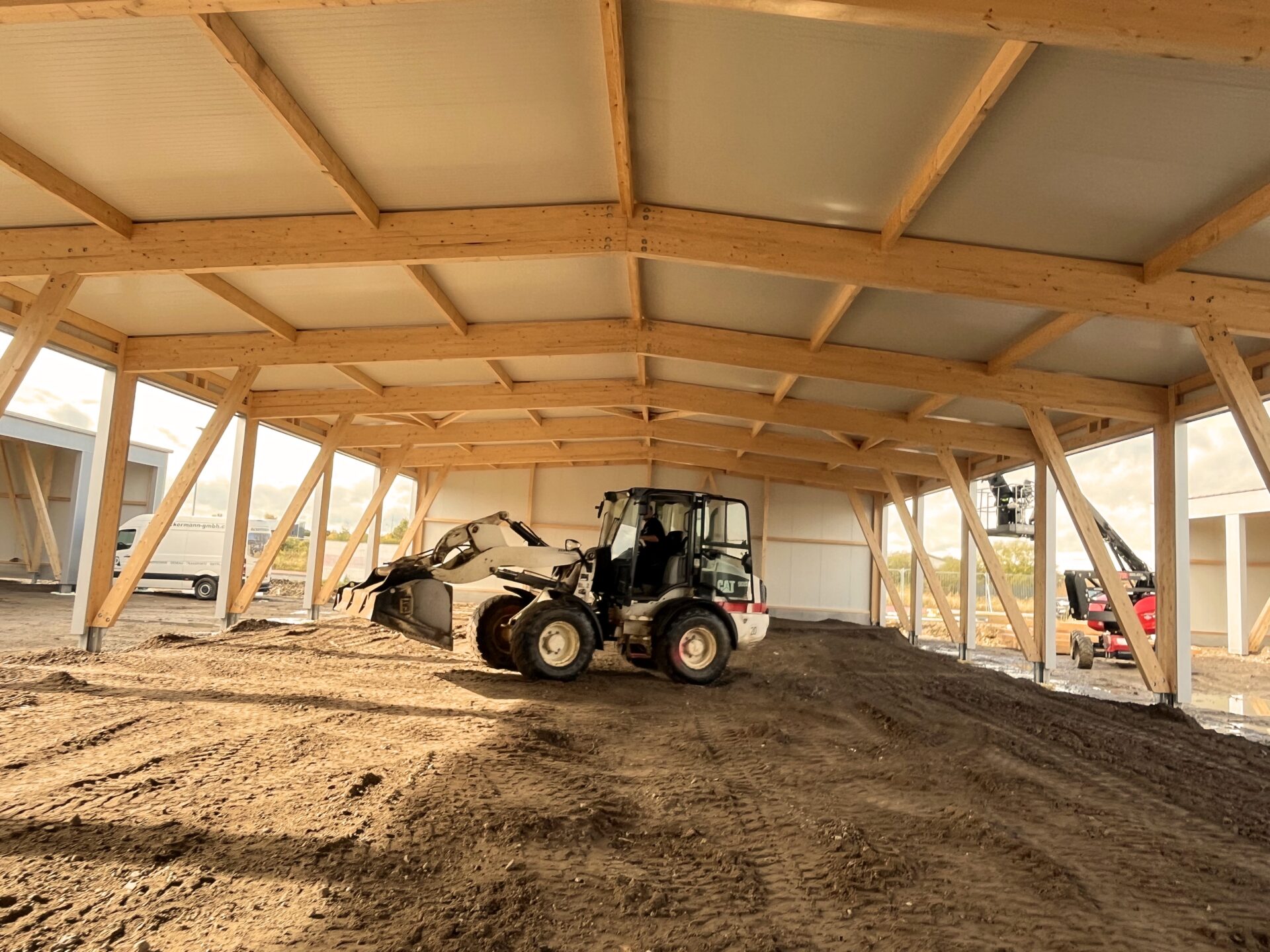 Radlader arbeitet unter Holzrahmenkonstruktion mit Dachbahn in Baustelle während Erdarbeiten.