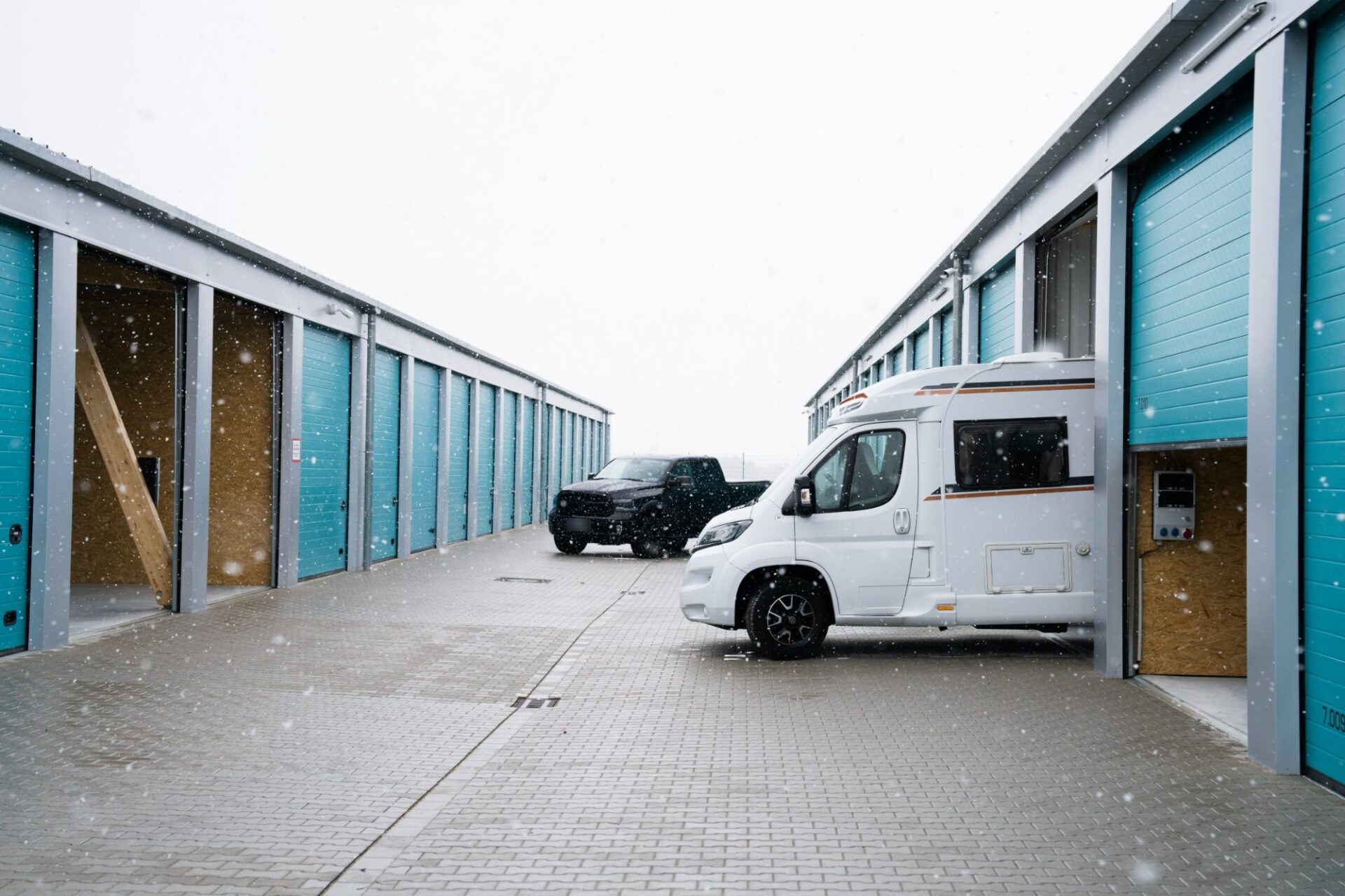 smartUP Garagenpark im Schnee mit Wohnmobil und Pick-up vor türkisfarbenen Rolltoren